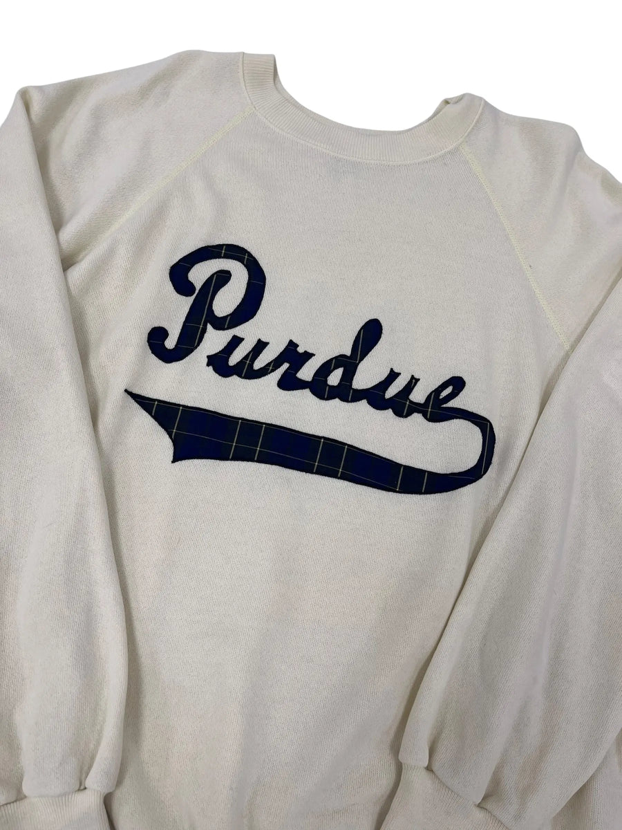 An off-white long-sleeve raglan sweatshirt featuring a navy blue 'Purdue' script graphic with a navy plaid accent on the letter 'U', shown against a plain white background.