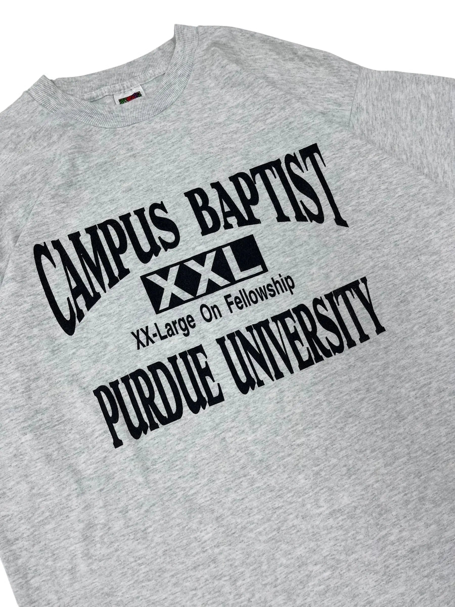 Close-up of a heather gray t-shirt featuring a black printed graphic for Purdue University Campus Baptist with a small red, white, and blue flag tag visible on the inside neck.